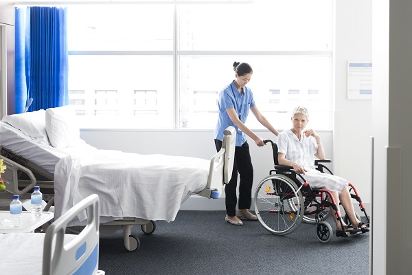 female patient in wheelchair on hospital ward. Disabled patient receiving help from female nurse.